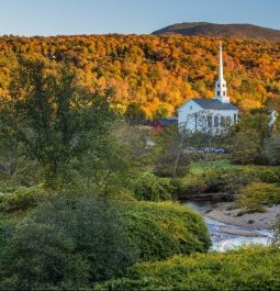 A white steeple church stands tall amongst the fall-hued tress in Stowe, Vermont