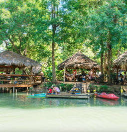 blue green water with colorful canoes on the shoreline with straw covered cabanas