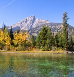 crystal-clear lake with mountain range peaking out behind fall foliage