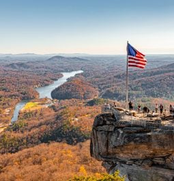 Mountaintop view of fall foliage with river and rock jutting out with American flag