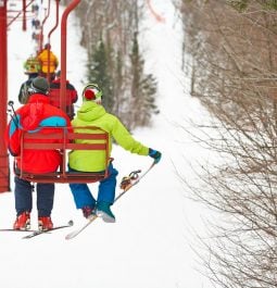 Two skiers in bright ski gear sitting on chairlift going up the mountain to ski