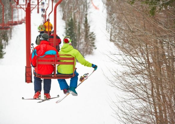 Two skiers in bright ski gear sitting on chairlift going up the mountain to ski