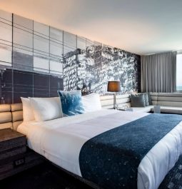 hotel room with white bedding and navy accents with mirrored wall behind the bed