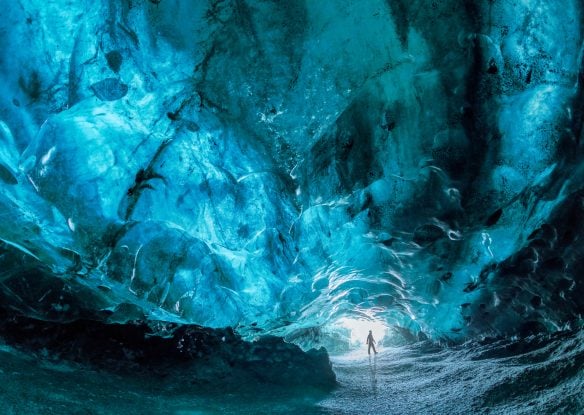 turquoise ice cave with person standing near entrance