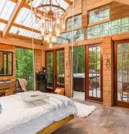 A chandelier and swing bed hang in the middle of a bedroom with floor-to-ceiling windows illuminating this Texas cabin