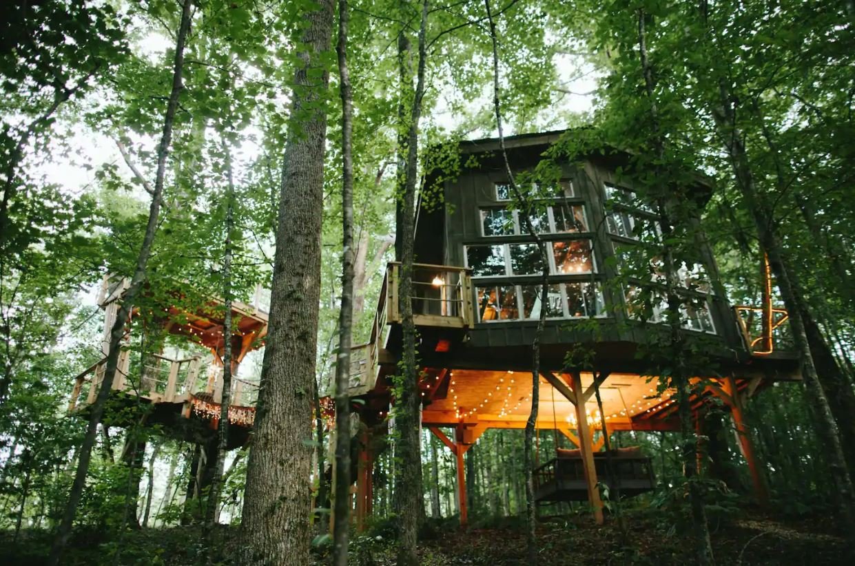 The exterior of The Majestic Treehouse with larger windows, a swing seat under the house tucked away on Bolt Farm