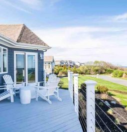The spacious deck of a blue beach house overlooks the ocean