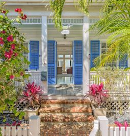 Brick pathway leading to Key West-style estate with blue shutters and tropical landscaping
