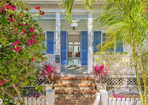 Brick pathway leading to Key West-style estate with blue shutters and tropical landscaping