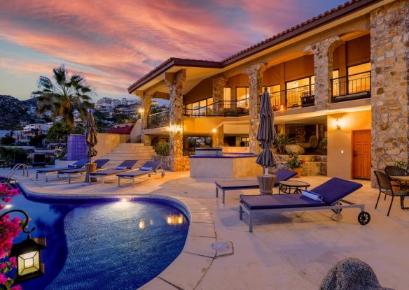 Back of stunning, large villa with stone accents and swimming pool facing Pacific