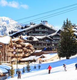 Ski resort with wooden chalets and skiings heading down mountain