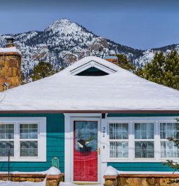 teal cottage with red door covered in snow with mountains in background