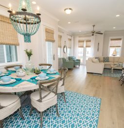 Dining table and chairs with cream seats, blue rugs and napkins, and cream couches in living area