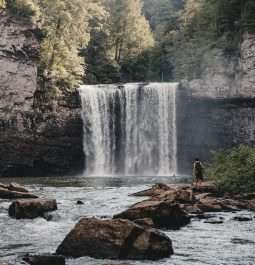 A person standing next to a small waterfall in the forests of Tennessee