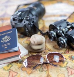 A camera, binoculars, sunglasses, passport and small travel book are spread out on a map.