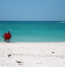 A man fishes by the beach in solitude on a clear, calm afternoon.