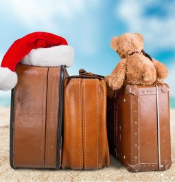 Set of family luggage with a stuffed bear and Santa hat on top sitting on a beach