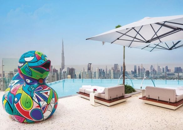 Rooftop pool overlooking dubai skyline with rubber duck art installation on pool deck