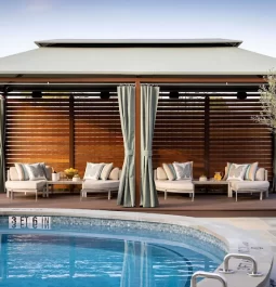 outdoor pool with cushioned lounge chairs under open air structure