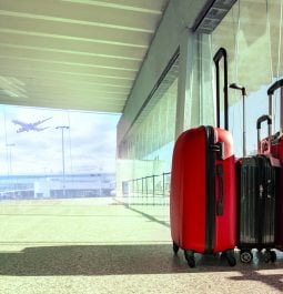 Three red suitcases sit in an empty terminal with floor to ceiling windows showing a plane taking off outside