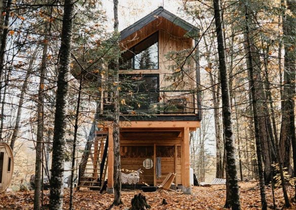 Exterior view of a treehouse with a wooden sauna nearby